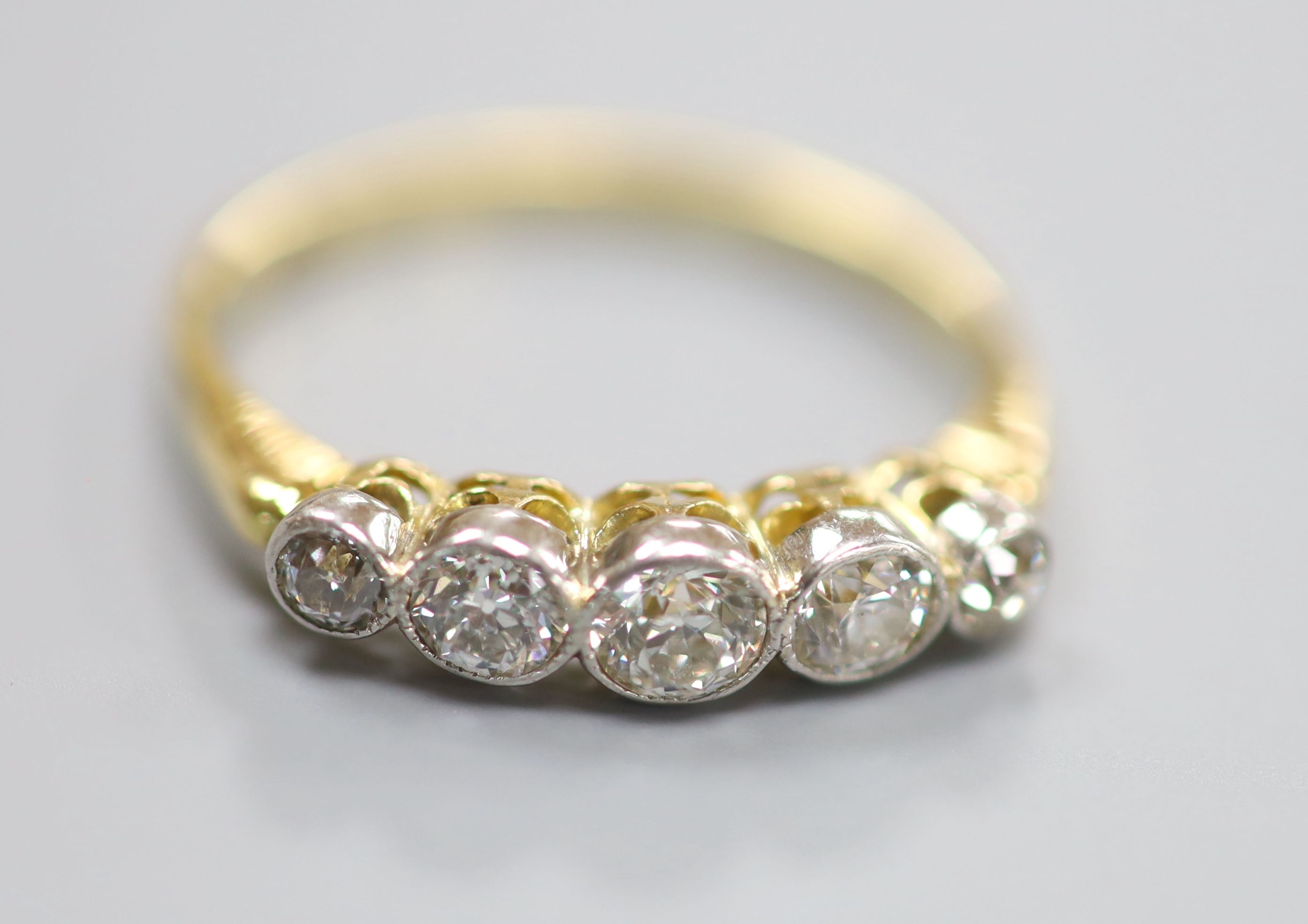 A yellow metal and graduated five stone diamond set half hoop ring, size P/Q, gross 2.6 grams.